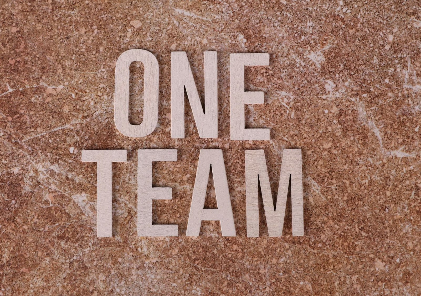 Wooden 'One Team' text on marble background symbolizing unity and teamwork.